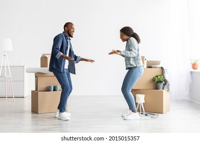 Happy Young Black Spouses Dancing In Their New Flat On Moving Day, Cheerful African American Couple Having Fun Among Cardboard Boxes With Belongings While Relocating To Own Apartment, Copy Space