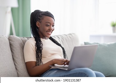 Happy Young Black Woman With Cute Hair Freelancer Working From Home, Sitting On Couch And Using Modern Laptop, Typing Text Or Communicating With Clients Online, Blogging Or Copywriting, Copy Space