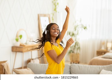 Happy Young Black Woman With Headphones And Mobile Device Dancing To Her Favorite Music At Home. African American Lady Moving To Beautiful Song, Having Great Time Indoos