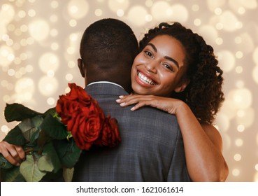 Happy young black woman holding red roses while hugging her man, having date outdoors. Happy Saint Valentine's Day