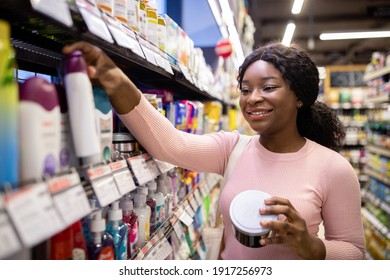 Happy Young Black Woman Shopping In Beauty Department Of Big Supermarket, Choosing Personal Care Products. Lovely African American Lady Buying Goods At Hygiene Section Of Mall