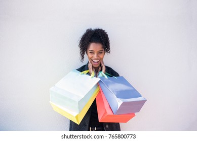 Happy young black woman with shopping bags against a white wall  