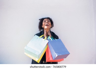 Happy young black woman with shopping bags against a white wall  