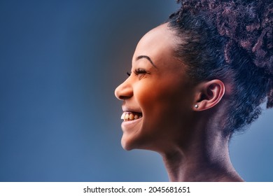 Happy young Black woman with a vivacious beaming smile posing in profile over blue in a close up cropped head shot