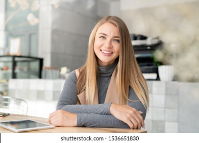 Happy young blond busineswoman in smart casualwear sitting by table in modern cafe in front of camera - Powered by Shutterstock