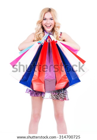 Happy young blonde woman with colored shopping bags in pink dress over white background.