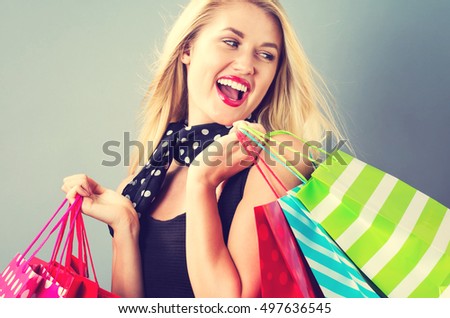 Happy young blonde woman with shopping bags on a gray background
