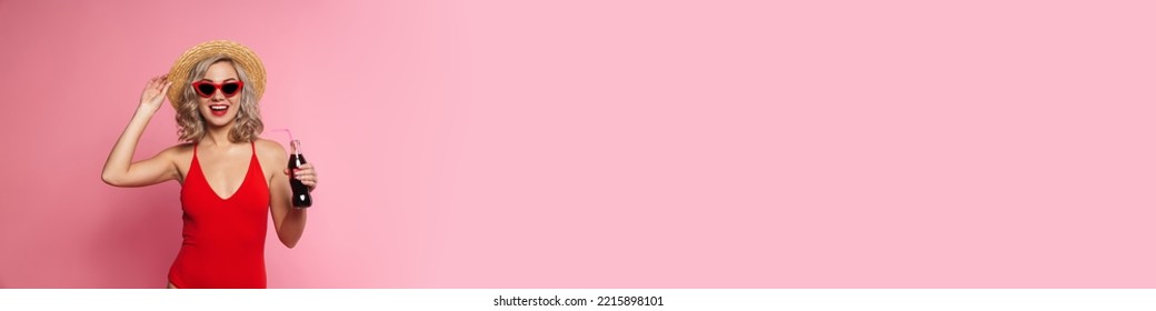 Happy Young Blonde Woman In Swimsuit And Sunglasses Holding Fizzy Drink Bottle Standing Posing Isolated Over Pink Background