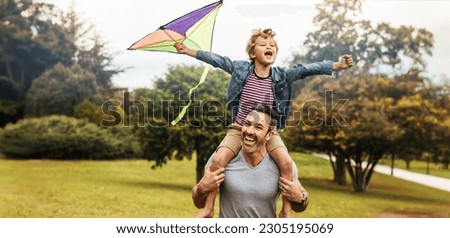 Happy young boy flying a kite while sitting on his father's shoulders, enjoying father's day out in the park. Dad and son bonding and having some outdoor fun during family time.