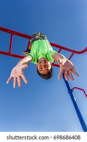 A Happy Young Boy Hangs Upside Down From The Monkey Bars.