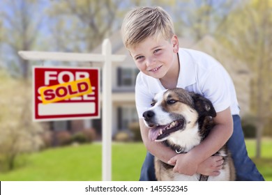 Happy Young Boy and His Dog in Front of Sold For Sale Real Estate Sign and House.