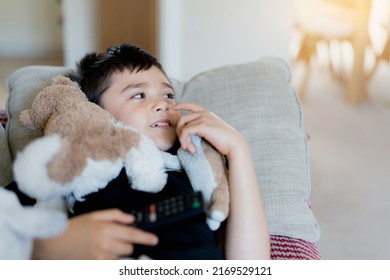 Happy Young Boy Holding Remote Control And Looking Up With Smiling Face, Cute Kid Lying On Sofa Enjoy Watching TV Program, Child Relaxing At Home On Weekend