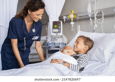 Happy young boy lying on gurney talking to friendly nurse. Smiling healthcare worker taking care of cute little boy lying on bed in hospital with IV drip. Paramedic tuck the covers back to the patient - Shutterstock ID 2147820697