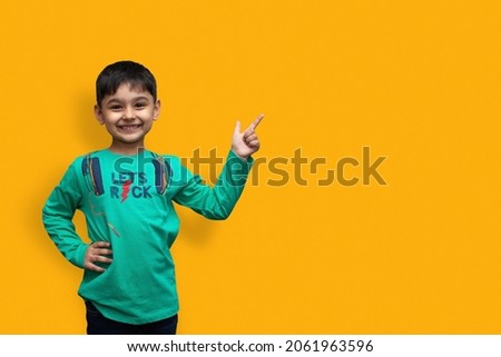 Happy young boy in shirt pointing up and holding arm white looking at the camera over isolated background and copy space