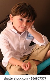 Happy Young Boy Sitting Cross Legged In A Chair Holding Wrapped Candy.