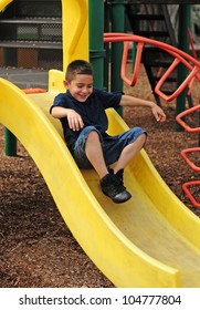 Happy young boy sliding down slide and having fun at outdoor park