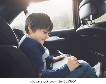 Happy young boy using tablet computer while sitting in the back passenger seat car and safety belt  Child boy drawing smart pad Portrait toddler entertaining him self road trip  