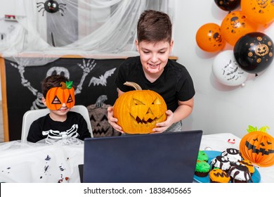 Happy young boys, brothers talking with grandparents or friends via video call using laptop on halloween day , excited kid showing his new Jack O' Lantern Halloween pumpkin with carved smile