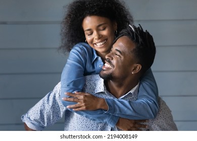 Happy young Brazilian ethnicity man giving piggyback ride to laughing beautiful African American wife, having fun together near grey wall, good trusted family relations, entertainment activity - Powered by Shutterstock