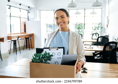 Happy Young Brazilian Or Hispanic Female Employee, Holding Cardboard Box, Standing In Modern Office And Looking At Camera, Smiling, Newcomer Woman Got New Job, Her First Day Of Work In New Workspace