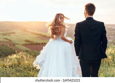 Happy young bride woman in white dress running in the sunset light with blowned hair. Back view.