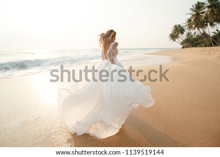 Happy young bride woman in white dress  running, have fun on clean sandy beach waves of azure sea or ocean on sunset, summer vacation at water. Wedding rest, relax honeymoon concept.