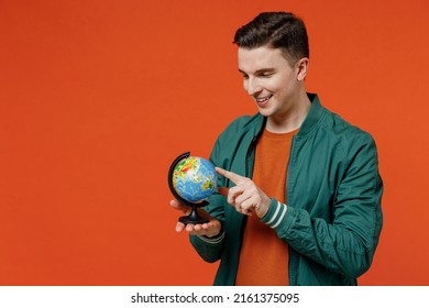 Happy Young Brunet Man 20s He Wear Red T-shirt Green Jacket Hold In Hands Point On Earth World Globe Isolated On Plain Orange Background Studio Portrait. Stop Nature Garbage Ecology Protection Concept