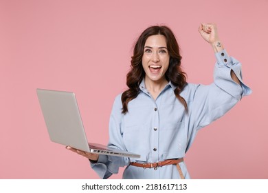 Happy young brunette woman 20s wearing casual blue shirt dress posing working on laptop pc computer doing winner gesture looking camera isolated on pastel pink colour background, studio portrait - Shutterstock ID 2181617113