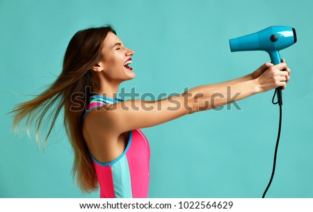 Happy young brunette woman with hair dryer on blue mint background. Hair style beauty concept