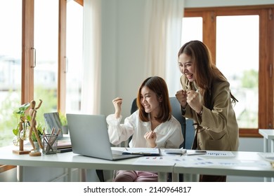 Happy Young Business Asian Team Looking At Laptop Screen, Celebrating Success, Raising Arms In A Celebration Of A Successful.