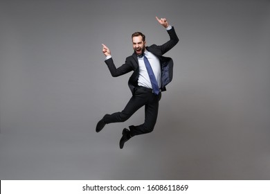 Happy young business man in classic black suit shirt tie posing isolated on grey background. Achievement career wealth business concept. Mock up copy space. Jumping, point index fingers up, screaming