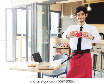 Happy young business man owner standing and showing red heart in modern cafe, service mind concept. Copy space.