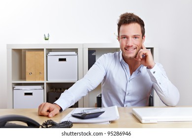 Happy Young Business Man Sitting At Desk In Office