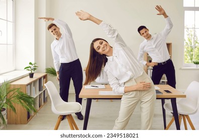 Happy young business people doing stretching sport exercises standing at the workplace in modern office. Group of smiling company employees exercising fitness for health during a break from a work. - Powered by Shutterstock