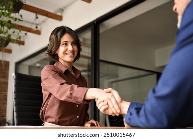 Happy young business woman bank manager handshaking client at meeting. Smiling female hr hiring recruit at job interview, insurance agent, lawyer making contract deal at work with business handshake.