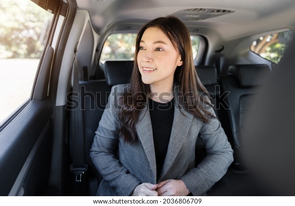 happy young business\
woman thinking and looking view out of window while sitting in the\
back seat of car 