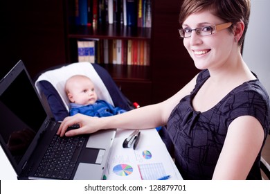 happy young business woman working on a laptop with her baby at the back