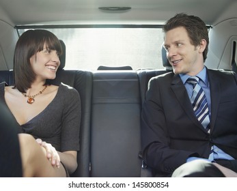 Happy Young Businessman And Businesswoman Talking In Back Seat Of Car