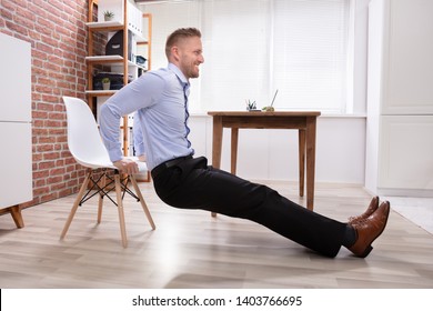 Happy Young Businessman Doing Triceps Dips In Office