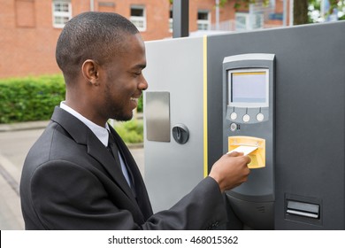 Happy Young Businessman Inserting Ticket Into Parking Machine To Pay For Parking