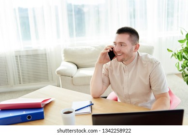 Happy young businessman sitting at wood desk, working on laptop and talking on mobile phone with client at home office, copy space - Shutterstock ID 1342258922