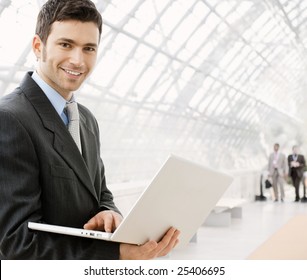 Happy young businessman using laptop in business building, smiling. - Powered by Shutterstock