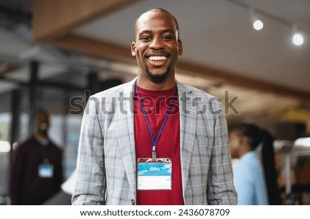 Happy young businessman wearing an ID badge at a professional expo. He smiles confidently, representing success, approachability, and positive corporate culture in a well-lit, modern venue.