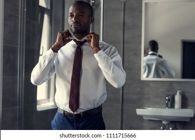 happy young businessman in white shirt putting on his tie at bathroom - Powered by Shutterstock