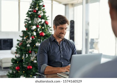 Happy young businessman working on laptop during christmas holiday. Successful business man in modern office working with xmas tree in background. Entrepreneur using laptop in modern office. - Powered by Shutterstock