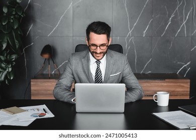 Happy young businessman working on laptop while sitting in modern office at the desk. E-learning e-commerce concept. Boss manager CEO doing report, typing official letter online at workplace - Powered by Shutterstock