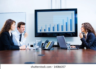 Happy Young Businesspeople Having Meeting In Boardroom At Office In Front Of A Huge Plasma TV Screen, Indoor, Smiling.