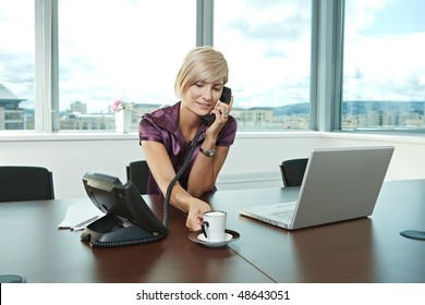 Happy Young Businesswoman Sitting At Table In Office Meeting Room, Talking On Phone, Smiling.