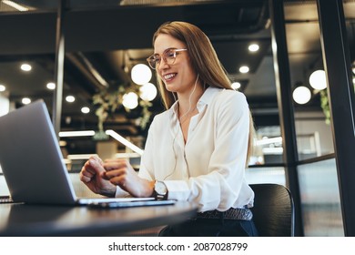 Happy young businesswoman taking a video call in a modern workspace. Young businesswoman smiling during a virtual meeting on her laptop. Cheerful female entrepreneur sitting at a table in an office. - Powered by Shutterstock