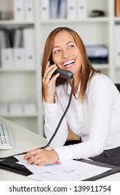 Happy Young Businesswoman Using Land Line Phone At Office Desk